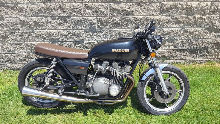 a black motorcycle parked on top of a lush green field next to a brick wall