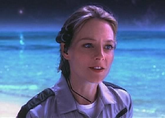 a woman in uniform standing on the beach looking off into the distance with water behind her