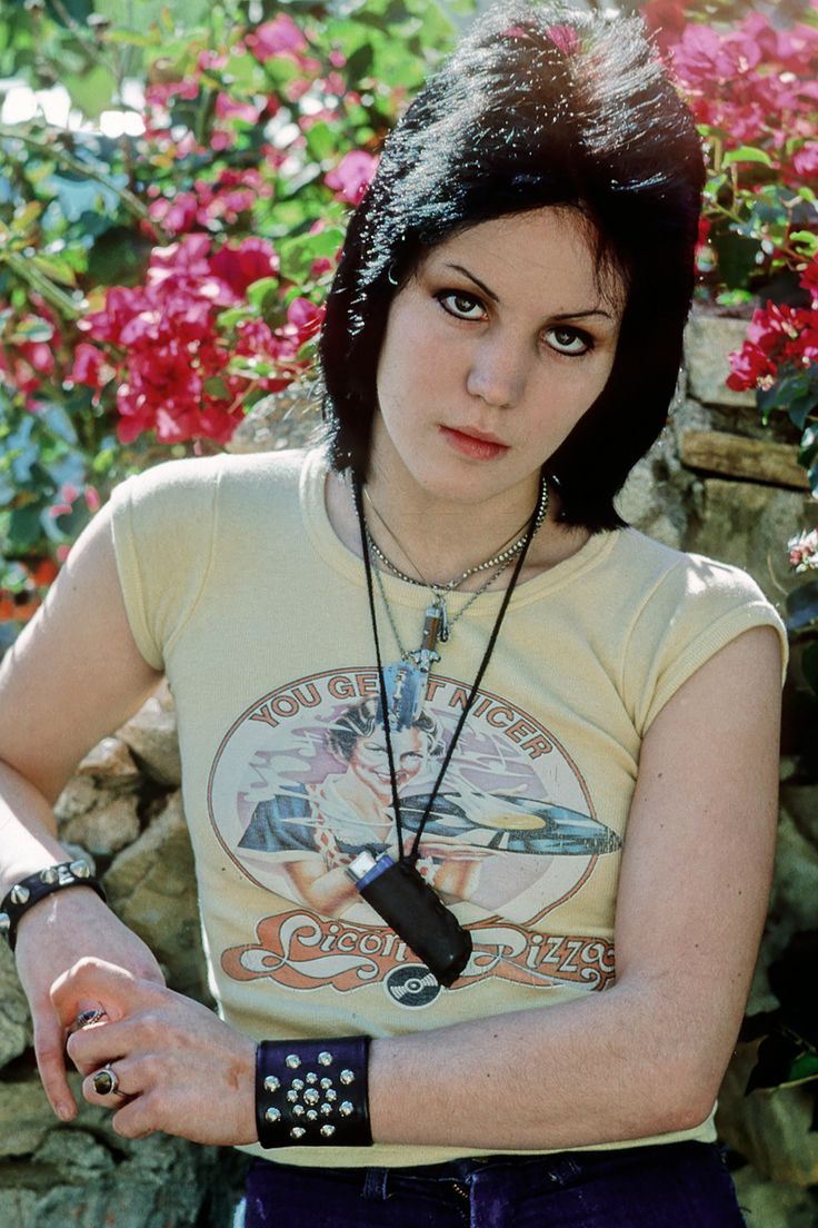 a woman with black hair wearing a yellow shirt and purple skirt standing in front of flowers