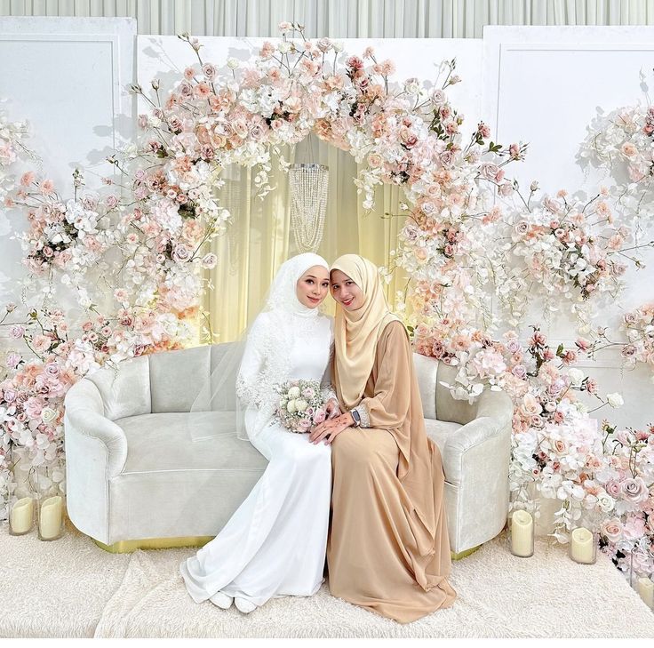 two women sitting next to each other in front of a floral backdrop with candles and flowers