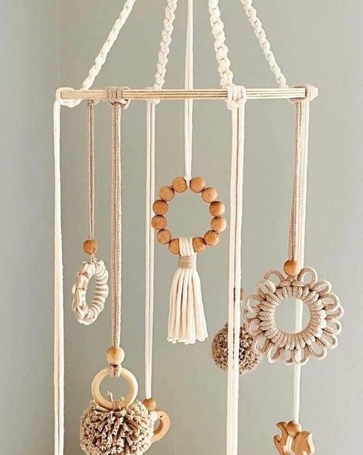 a white mobile with beads and tassels hanging from it's sides in front of a gray wall