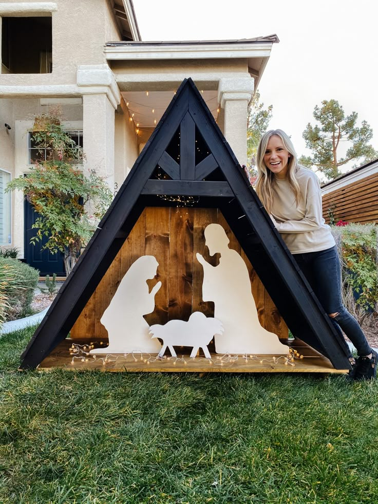 a woman standing next to a nativity scene in front of a house with christmas lights