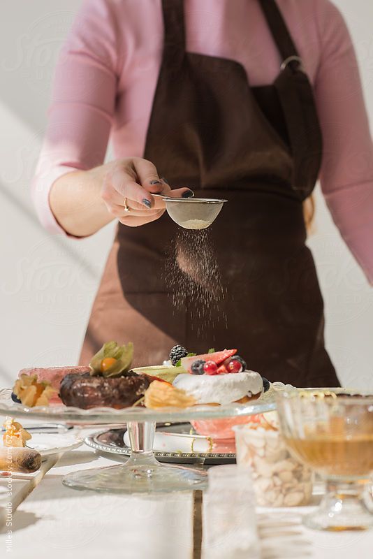 a woman in an apron sprinkling sugar on food