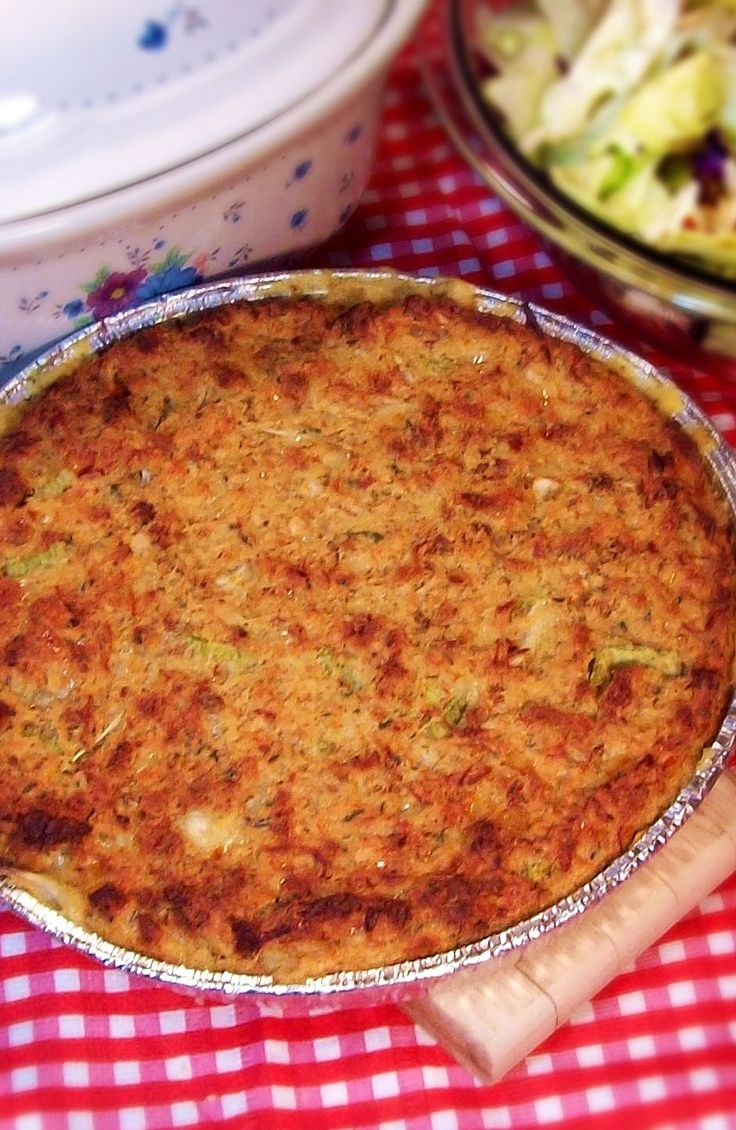 a pie sitting on top of a red and white checkered table cloth next to a bowl of salad