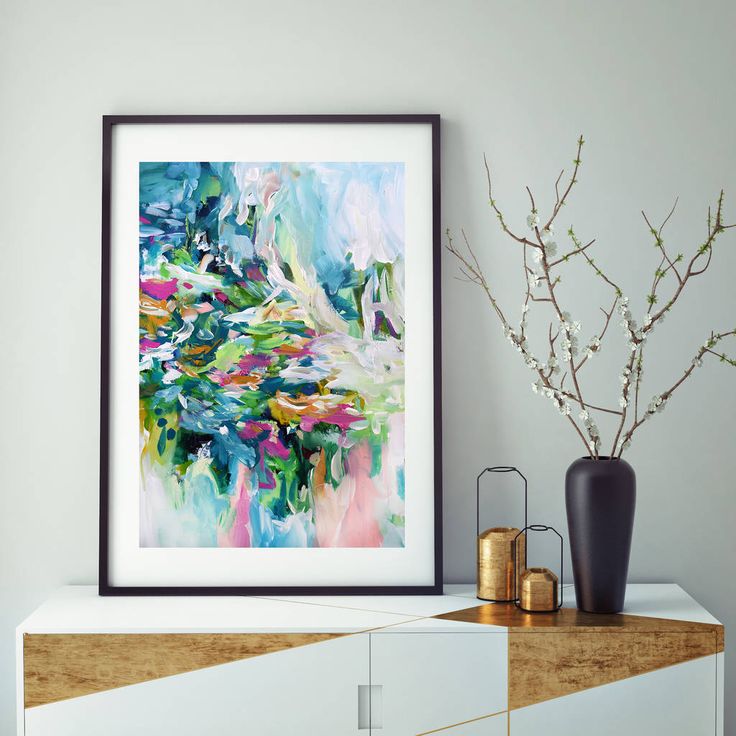 an abstract painting is displayed on the wall next to a vase with flowers in it