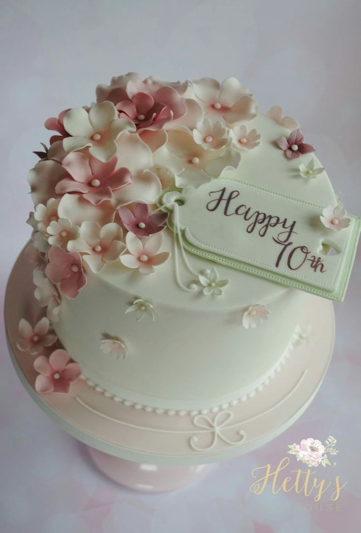 a white cake with pink flowers on top and a happy 10th sign in the middle