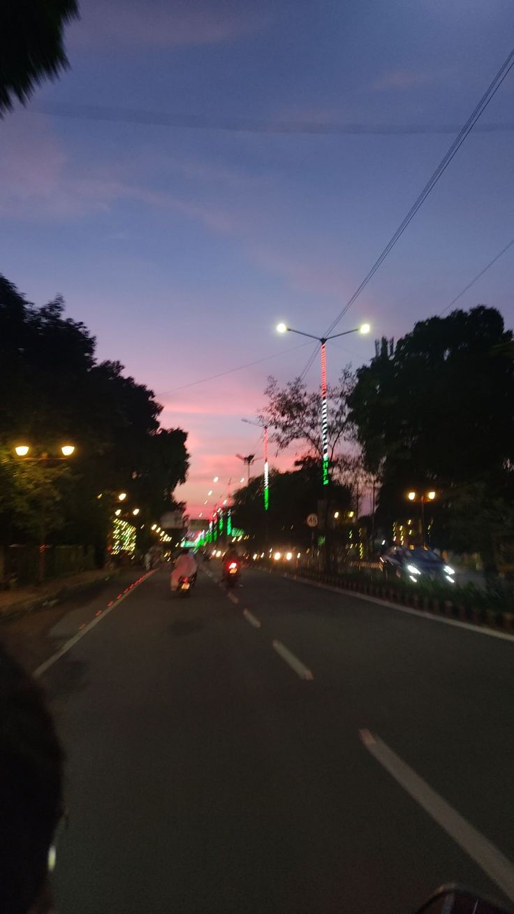 people riding motorcycles down the street at night with green lights on poles in the distance