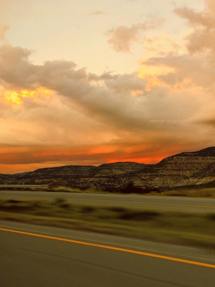 the sun is setting over the mountains as seen from a moving car on the highway