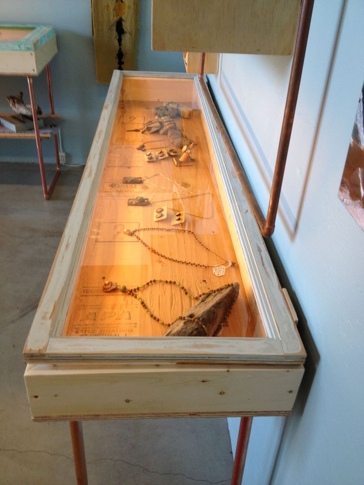 a wooden table topped with lots of different types of necklaces on display next to a wall