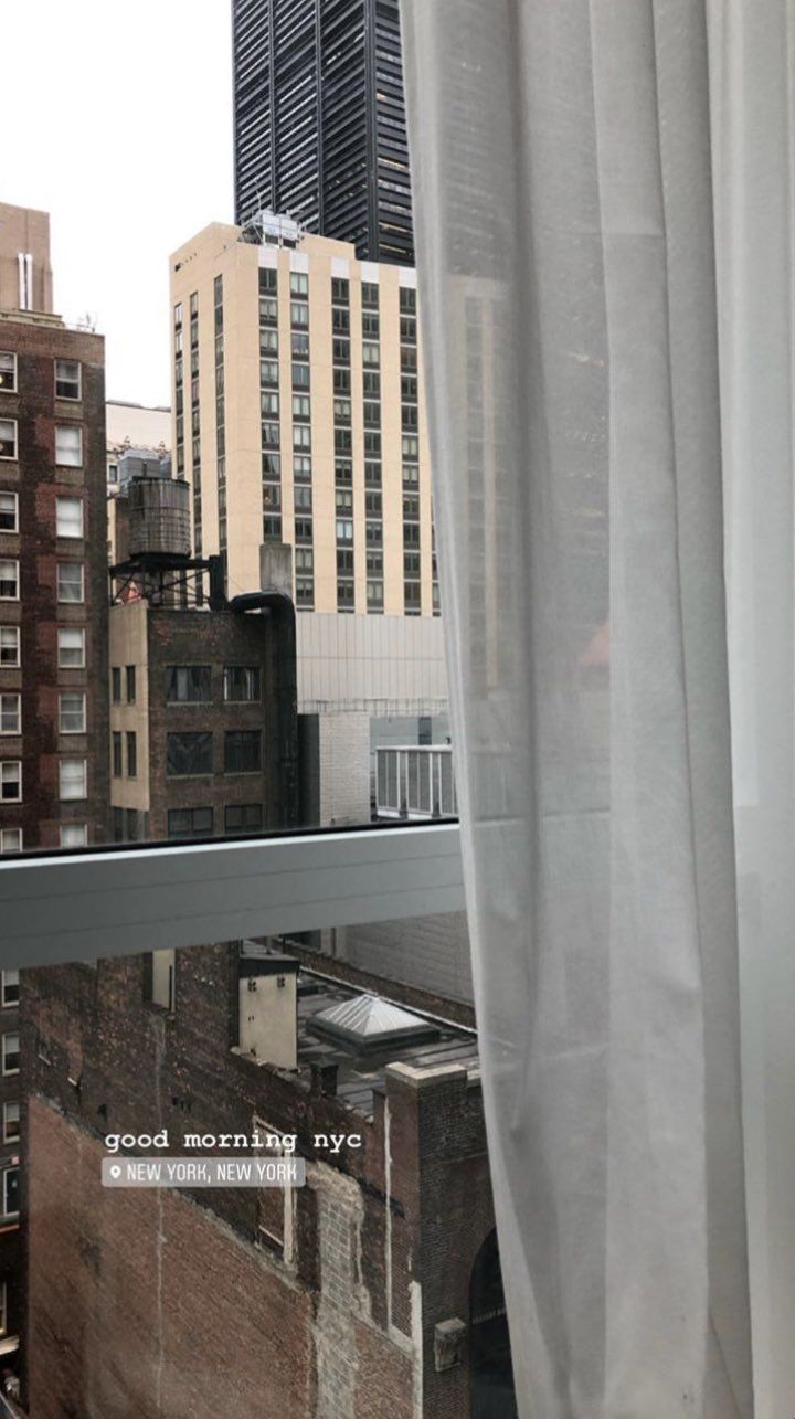 an open window with white curtains in front of tall buildings and skyscrapers on the other side