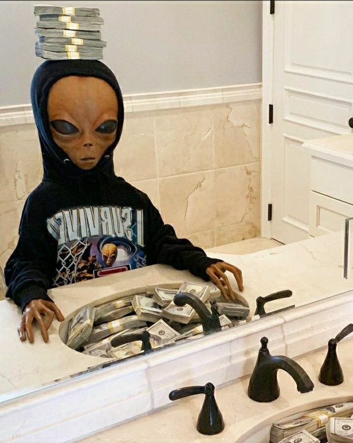 an alien in a black hoodie sitting at a sink with several faucets on it