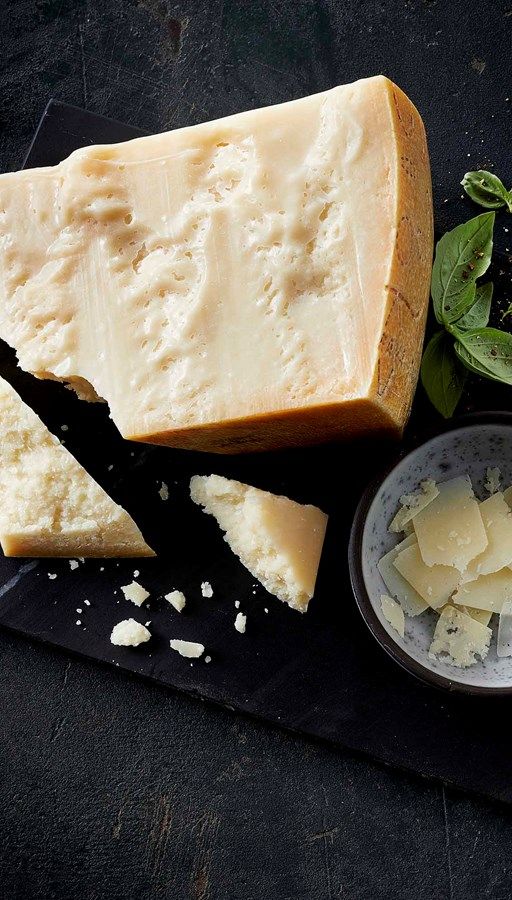 some cheese is sitting on a black board next to a small bowl with basil leaves