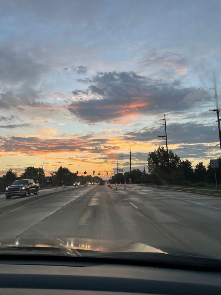 the sun is setting on an empty highway with cars driving down it and trees in the distance