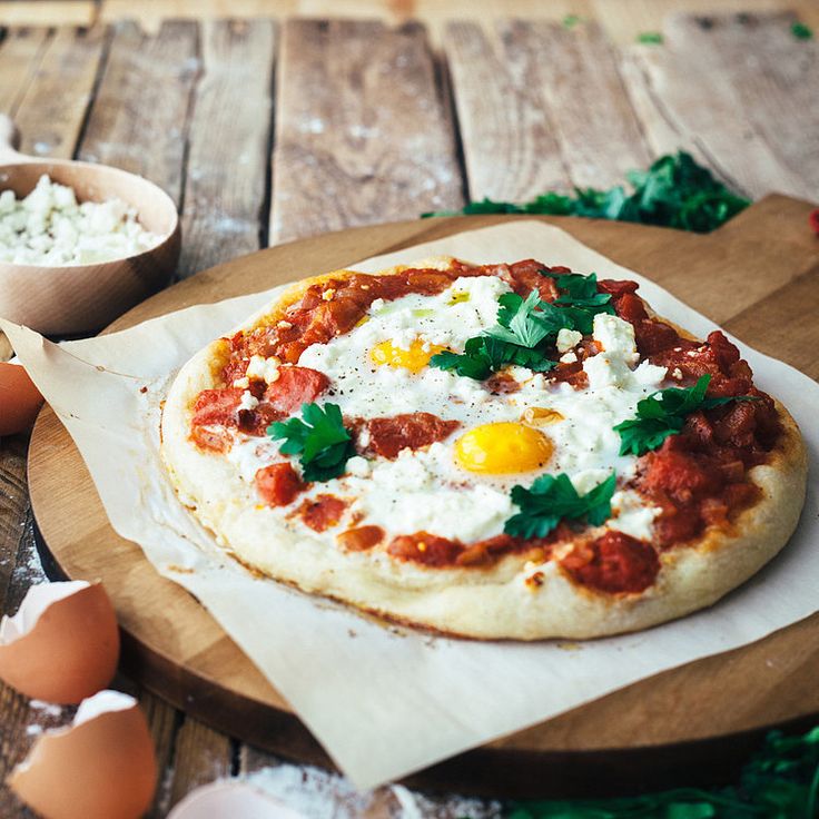 a pizza sitting on top of a wooden cutting board next to eggs and other ingredients