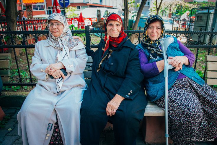 three women are sitting on a bench in the park and one is holding a cane