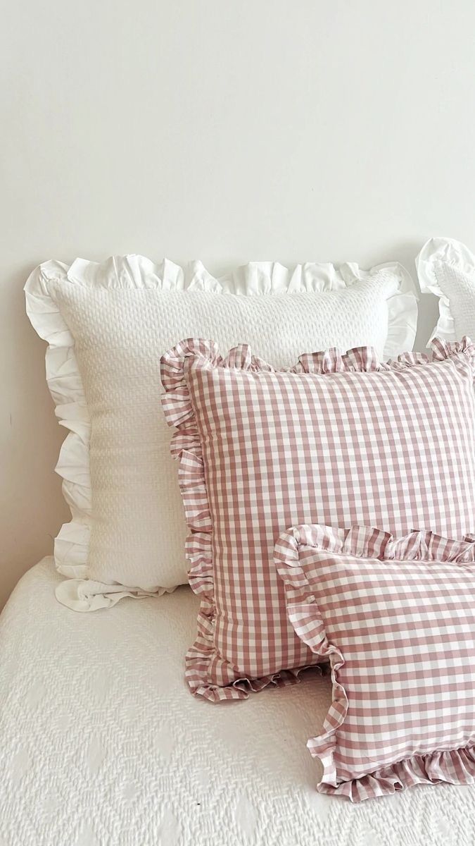 three pillows on top of a bed with white sheets and ruffled trimmings