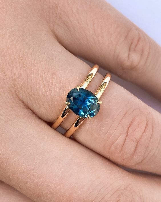 a woman's hand with two gold rings and a blue topazte ring