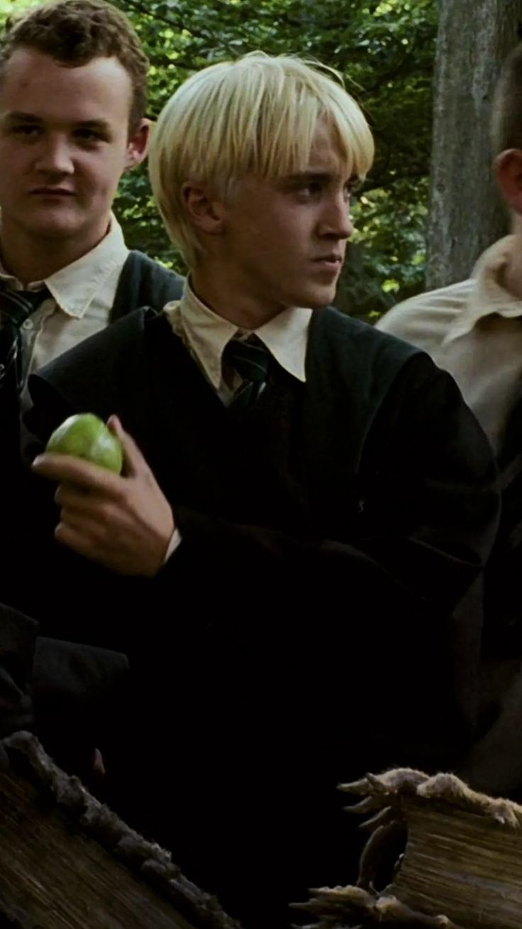 three young men in school uniforms standing next to each other, one holding an apple