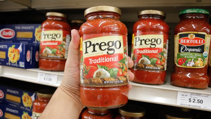 a hand holding a jar of prego traditional tomato sauce in front of other jars