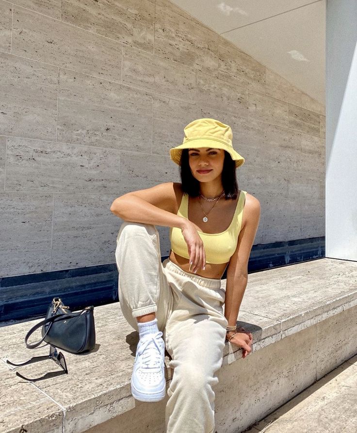 a woman sitting on some steps wearing a yellow hat and white pants with her legs crossed