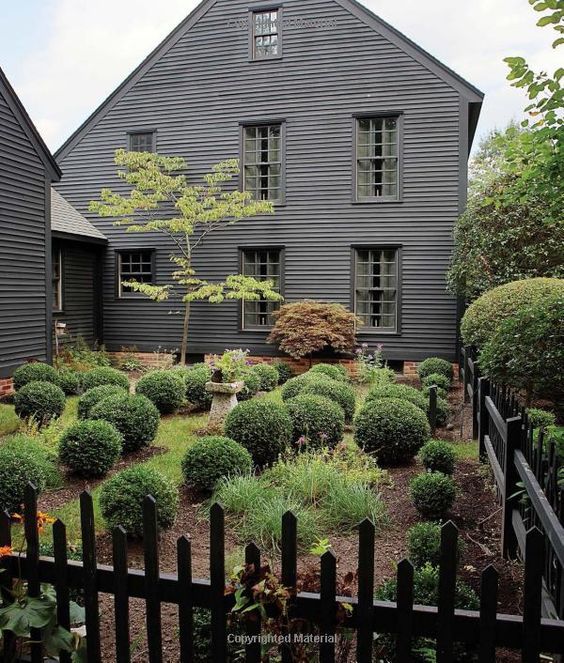 a black house with lots of trees and bushes around it