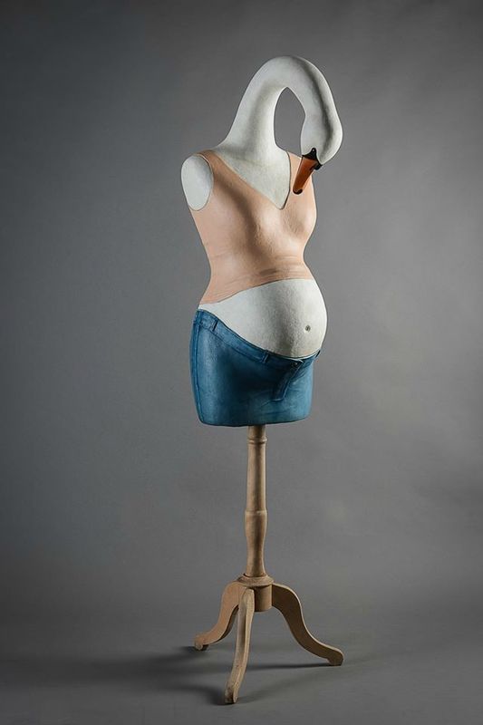 a mannequin's torso on a wooden stand in front of a gray background