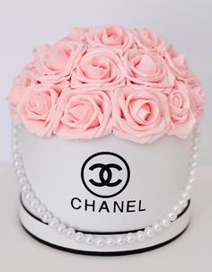 a chanel hat with pink roses and pearls around the top is shown on a white table