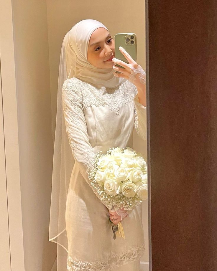 a woman in a wedding dress taking a selfie with her cell phone while holding a bouquet of flowers