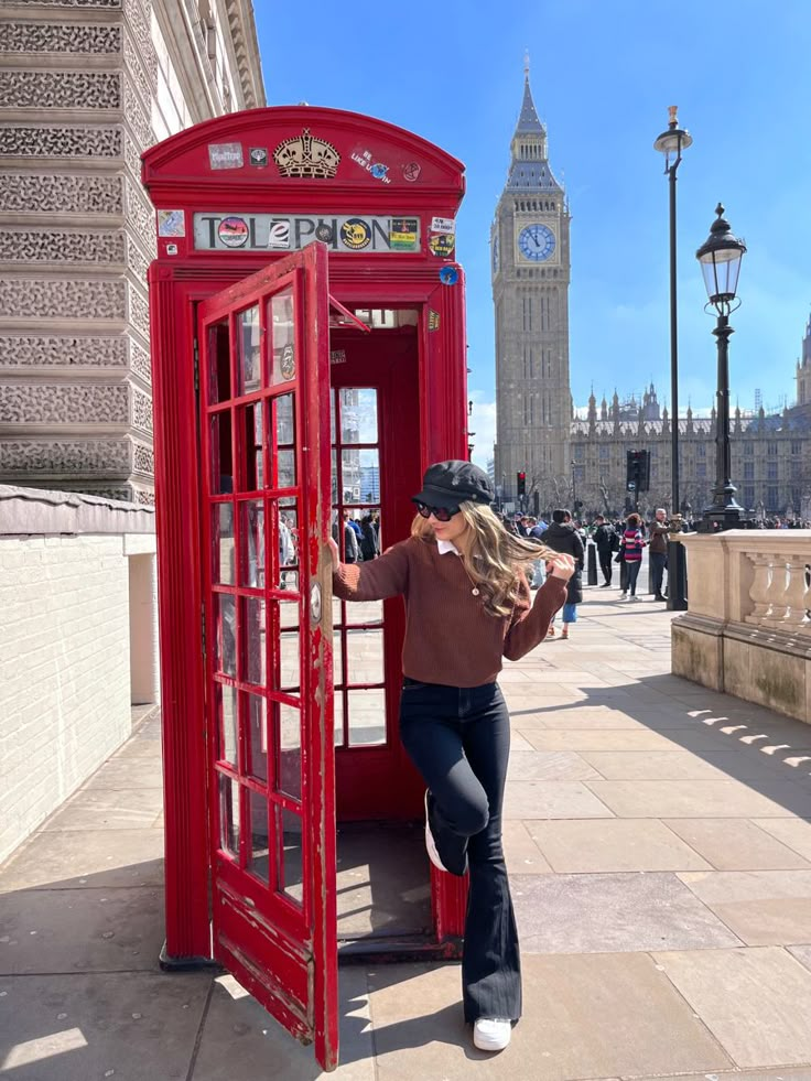 a woman leaning against a red phone booth on the sidewalk in front of big ben