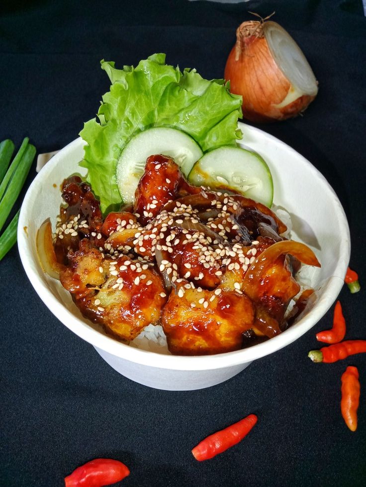 a white bowl filled with meat and vegetables next to green onions, cucumbers and carrots