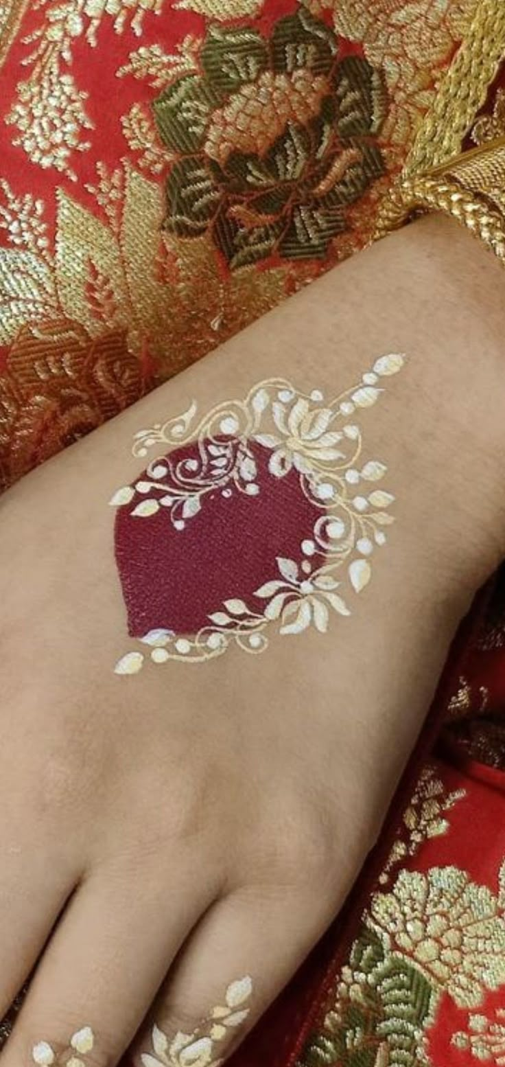 a woman's hand with white and red designs on her arm, which is covered in gold foil