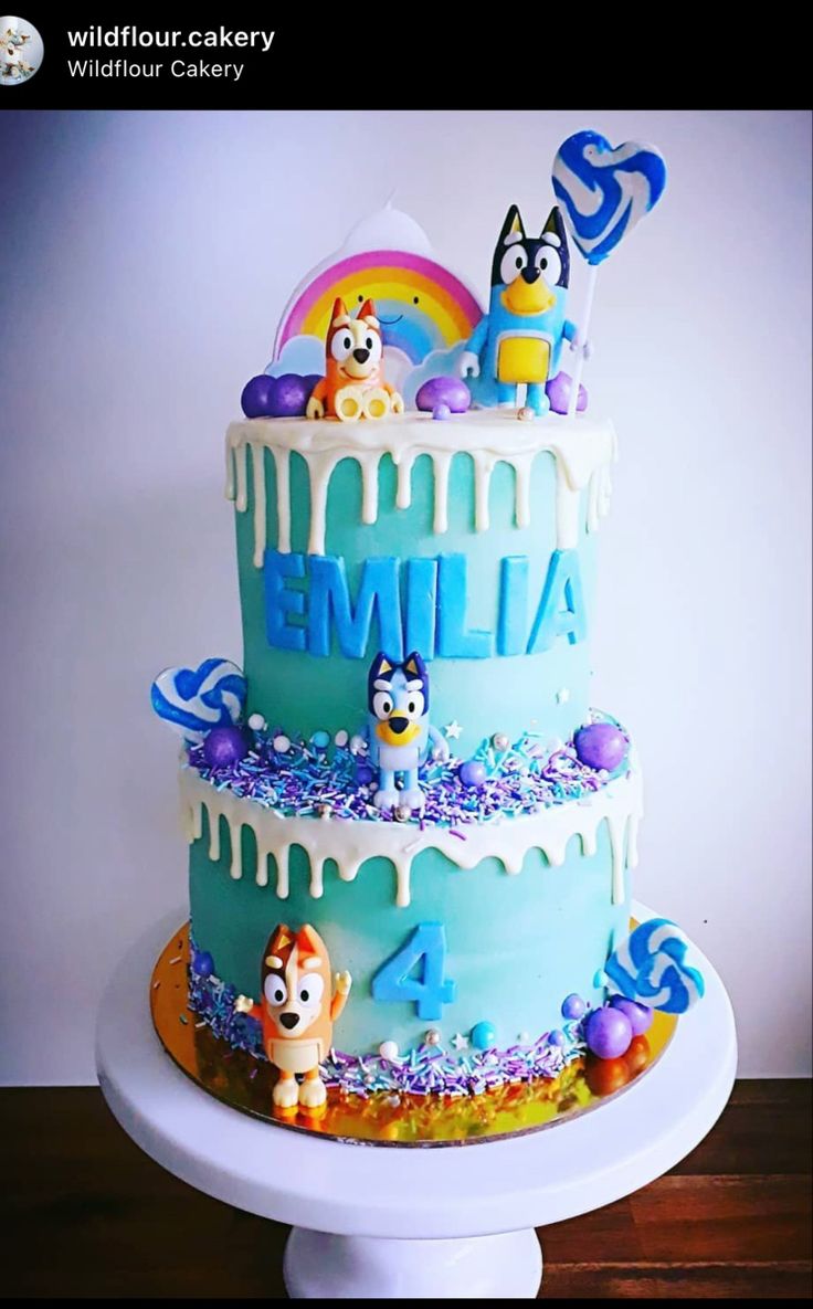 a three tiered cake with cartoon characters on the top and blue icing, sitting on a white pedestal