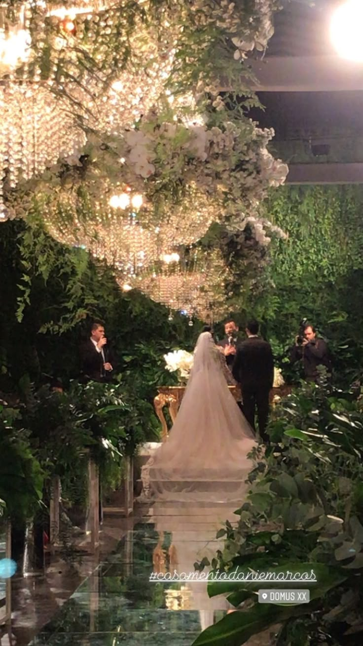 the bride and groom are walking down the aisle at their wedding ceremony, surrounded by greenery