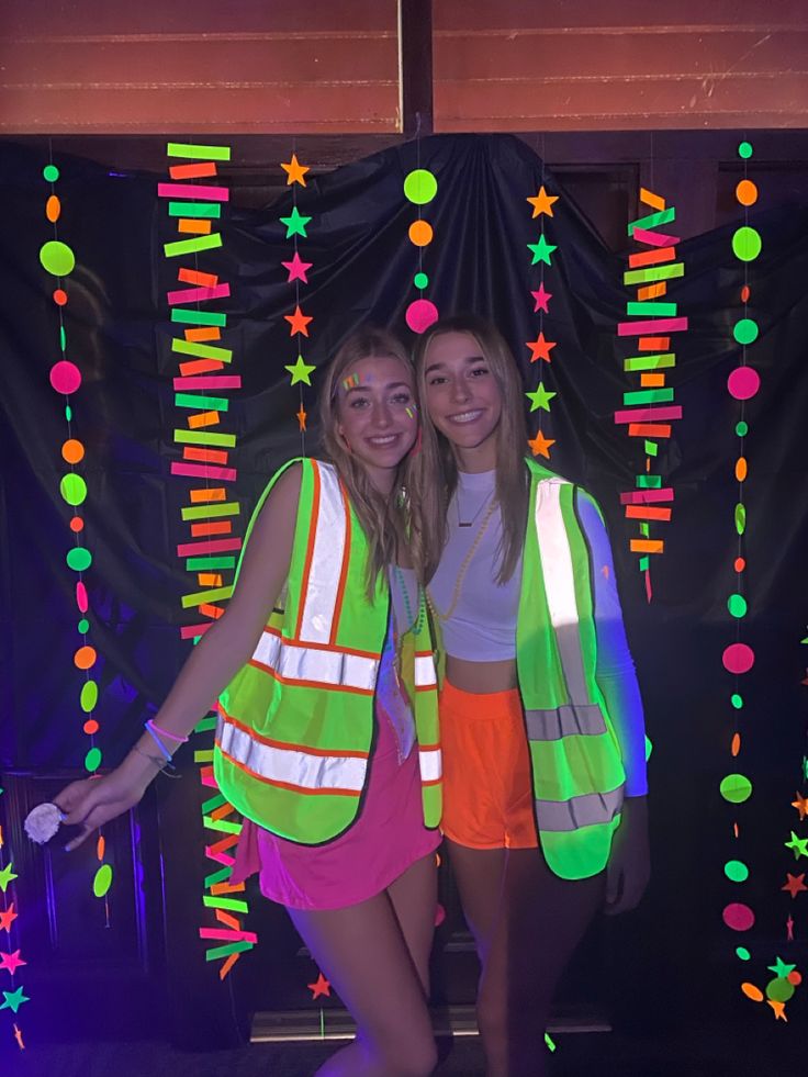 two young women standing next to each other in front of a wall with neon lights