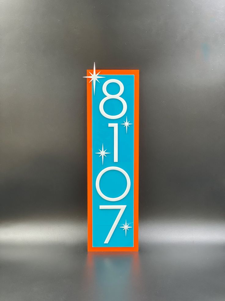 an orange and blue door number sign on a stainless steel surface with stars in the background