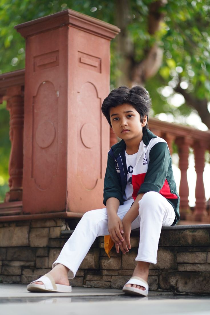 a young boy sitting on top of a stone wall next to a red planter