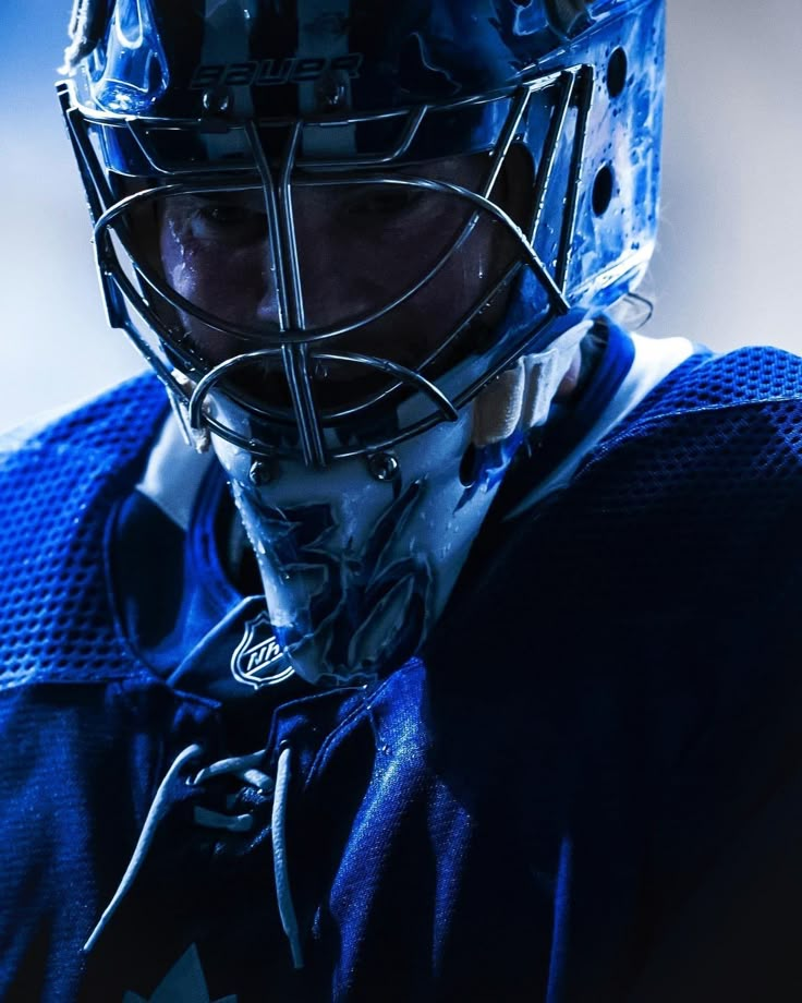 a close up of a hockey goalie's face wearing a blue uniform and helmet