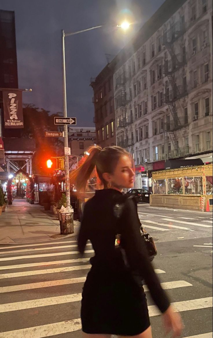 a woman crossing the street at night in a short dress and high heeled boots