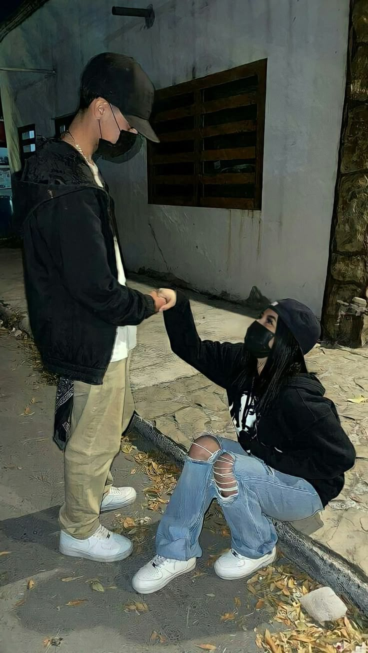 two people sitting on the ground with one person touching another's hand and wearing a mask