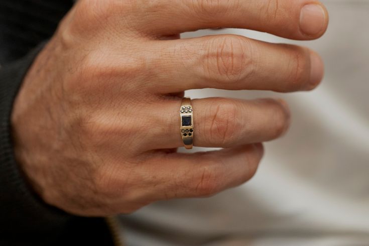 a man's hand wearing a gold ring with black stones on the middle finger