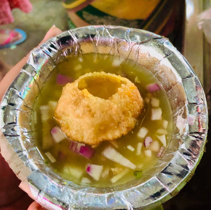 a person holding a bowl filled with soup and a small piece of food in it