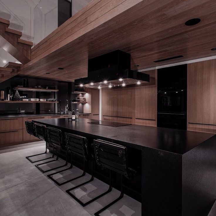 a large kitchen with black counter tops and wooden cabinets, along with stairs leading up to the second floor