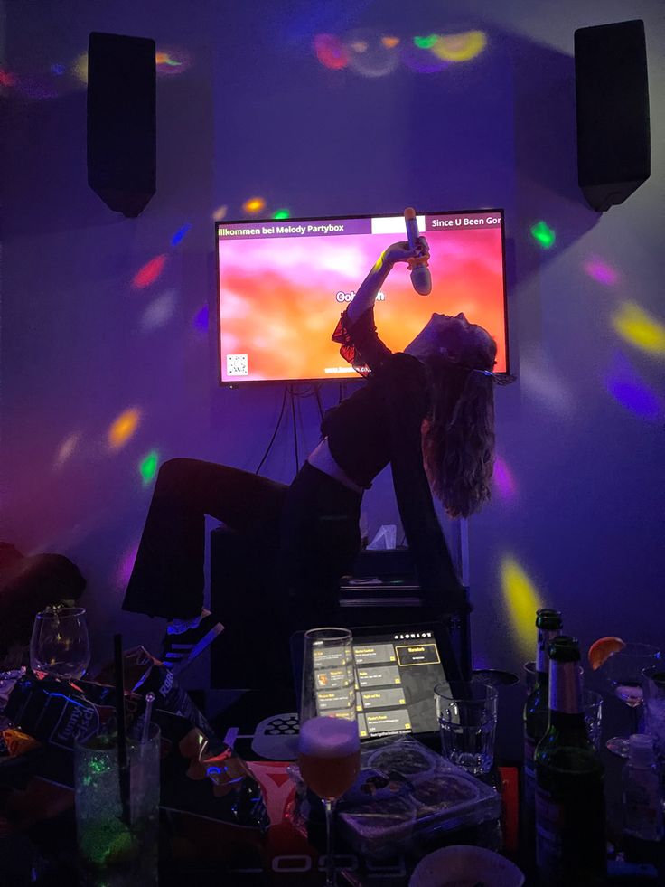 a woman is dancing in front of a tv with colorful lights on the wall behind her