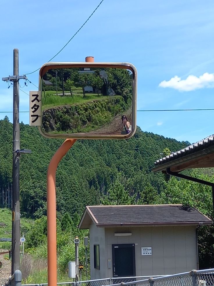 there is a mirror on the side of a pole near a building and mountains in the background