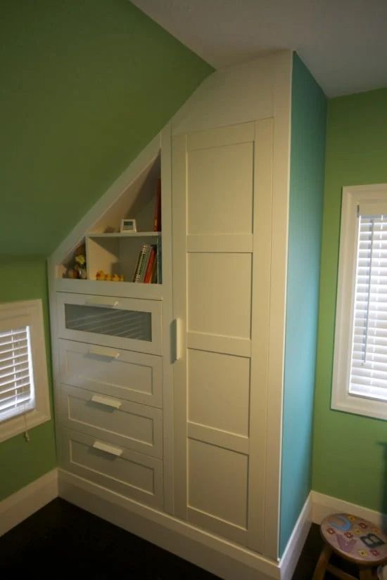 an attic bedroom with green walls and white drawers