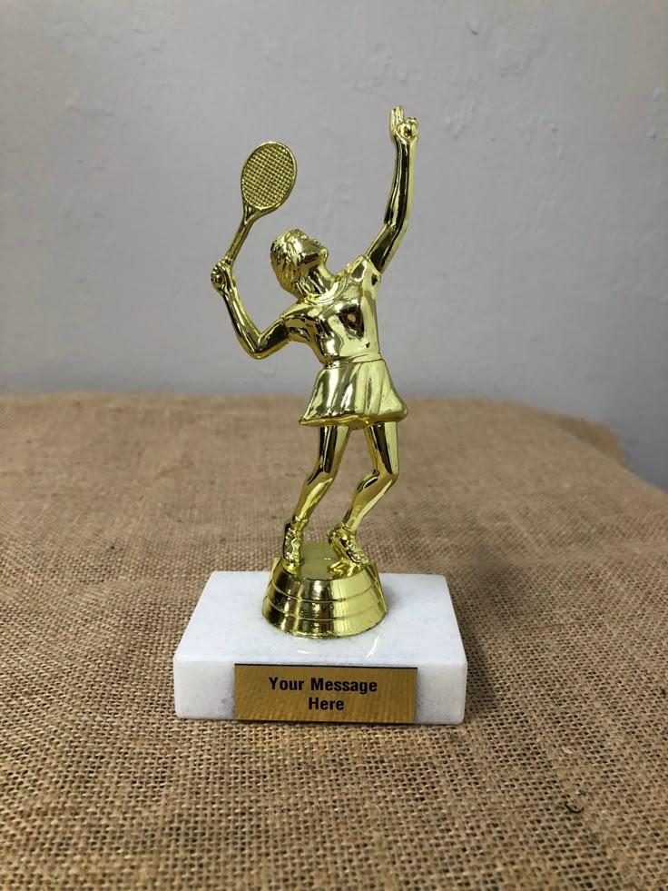 a gold statue holding a tennis racquet on top of a white base