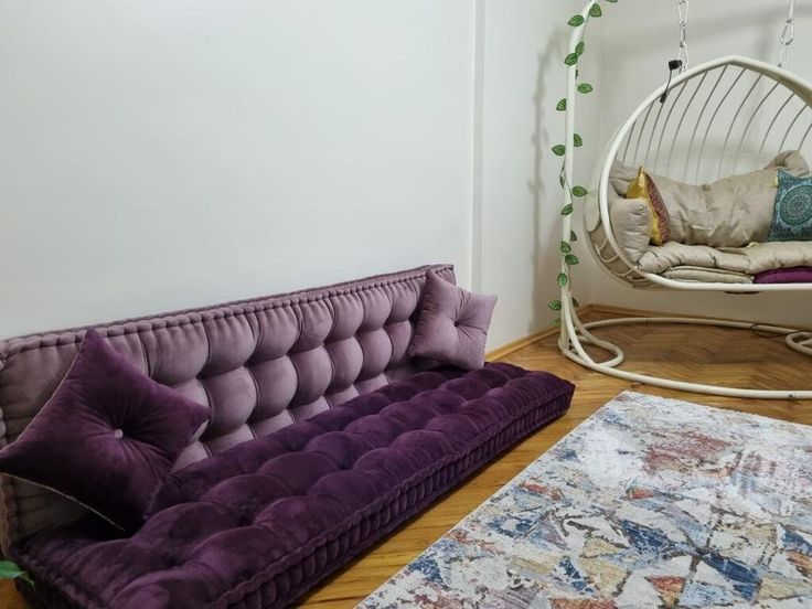 a purple couch sitting on top of a wooden floor next to a white swing chair