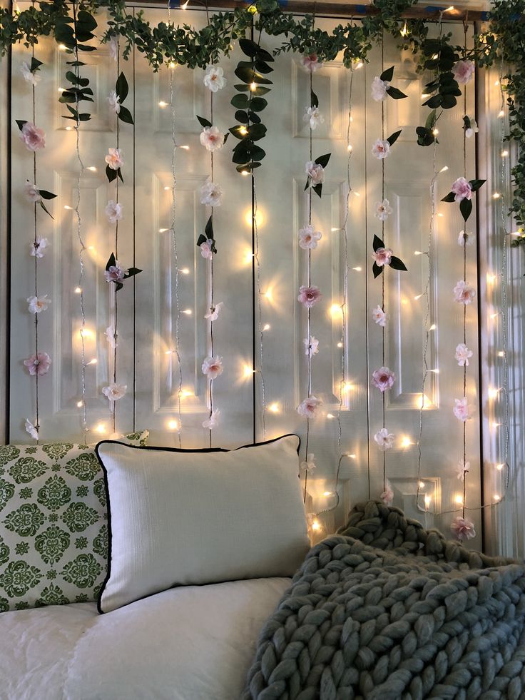 a bed covered in pillows and lights next to a wall with flowers hanging from it