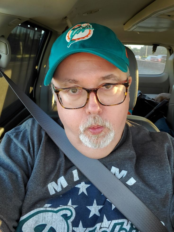 a man in glasses and a hat sitting in the back seat of a car with his head up