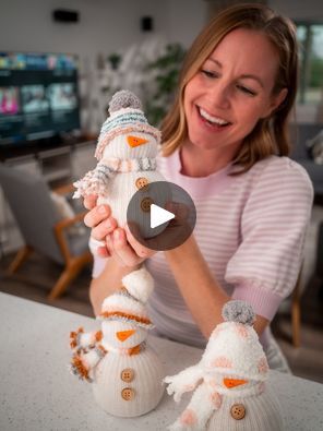 a woman holding two knitted snowmen on top of a white counter next to a tv